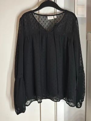Svart transparent blus från Vila - Snygg svart blus från Vila i transparent material med diskret prickmönster. Blusen har v-ringning, långa ärmar med volangdetaljer och spetsinslag vid axlarna. Hör av dig vid frågor!🥰✨ Nypris 349 kr🤍✨