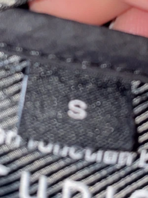 Svart pufferjacka med huva, stl S - Säljer en svart pufferjacka i storlek S med huva. Jackan har en stilren design och är perfekt för vårdagar. Passar dig som gillar en enkel men snygg look. Dragkedja framtill och sidofickor.