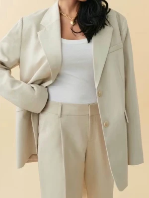 Beige kostym med kavaj och byxa - Stilren beige kostym med oversized kavaj och raka kostymbyxor. Kavajen har klassisk krage, knappar framtill och en fickdetalj. Byxorna har hög midja och vida ben. Perfekt för en trendig och clean look.