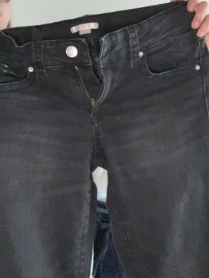 Svarta  jeans  - Säljer ett par svarta jeans med lätt tvättade detaljer och klassisk femficksmodell. Jeansen har silverfärgade knappar och dragkedja samt en snygg bakficka med knapp. Perfekta till en avslappnad streetstyle-look. Från Gina 