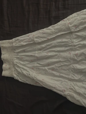 Vit blommig långkljol! - Romantisk vit långklänning med små blommor i rosa och blått. Klänningen har smock upptill och ett luftigt fall, perfekt för varma dagar. Materialet känns lätt och mjukt mot huden. Söt och feminin stil som passar till många tillfällen.