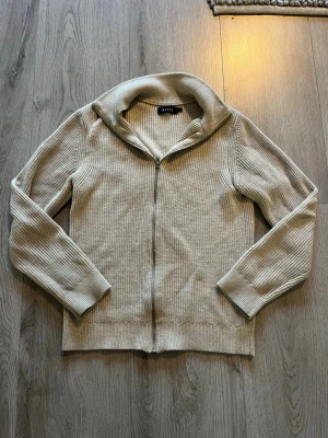 Beige stickad halvzip från Riley - Snygg beige stickad tröja från Riley med halv dragkedja och hög krage. Perfekt för lager-på-lager och passar till det mesta. Ribbstickad struktur ger en clean och stilren look. Den är från Brothers och jag köpte den för 1000 kronor. Säljer den för 499