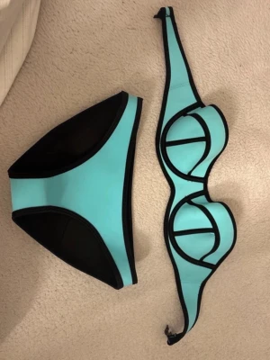 Turkos och svart bikini med bygel - Snygg bikini i turkos och svart med markerade svarta kanter och bygel i toppen. Bikinin har en modern, sportig look och är tillverkad i ett stretchigt material som passar perfekt för sommaren och strandhäng.