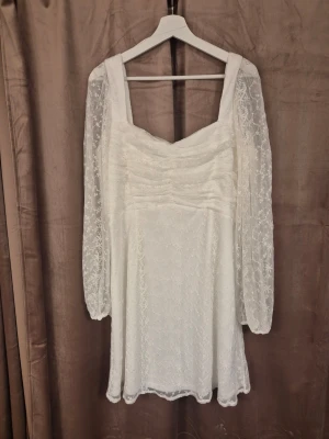 Vit spetsklänning med puffärmar - Söt vit kortklänning med transparenta långärmade puffärmar i spets. Klänningen har fyrkantig urringning, rynkade detaljer över bysten och ett lätt utställt kjolparti. Perfekt för dig som vill ha den perfekta studentklänning. Den har inga prislappar och alla lappar är avklippta men har aldrig använt, endast provat. 100 cm mått runt bysten, den är strechig vid magen och klänningen går ner till ca 12 cm ovanför knäna.