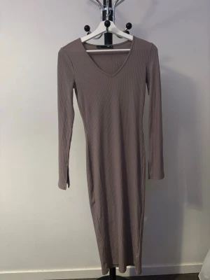 Beige ribbad långklänning  - Säljer en beige ribbad långklänning från 157 i storlek XS. Klänningen har v-ringning och långa ärmar, perfekt för en stilren och enkel look. Materialet är stretchigt och följsamt, vilket gör den bekväm att bära hela dagen.