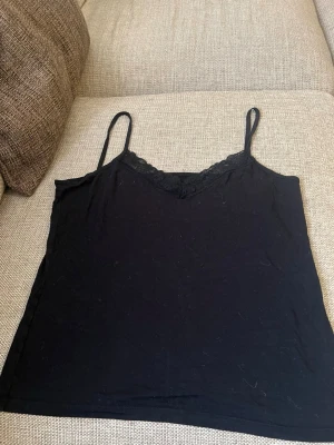 Svart spetsdetaljerad linnetopp - Snygg svart linnetopp med tunna axelband och spetsdetalj vid urringningen. Perfekt att styla lager på lager eller bära som den är. Enkel och stilren design som passar till det mesta.💞