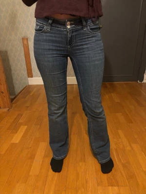 Bootcut jeans med kontrastsömmar - Mörkblå bootcut jeans med snygga kontrastsömmar och dekorativa bakfickor med zigzag-mönster. Klassisk femficksmodell och låg midja. Perfekta för en avslappnad och trendig look.