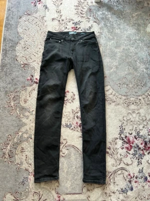 Svarta skinny jeans - Säljer ett par mörk grå skinny jeans med klassisk femficksdesign och smal passform. Jeansen har normal midja och raka ben. Perfekta för dig som gillar en stilren och enkel look. Materialet känns mjukt och stretchigt för extra komfort.