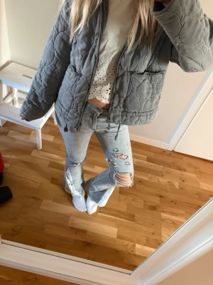 Ljusgrå slitna bootcut jeans med spets  - Säljer ett par ljusgrå jeans med bootcut-modell och rejäla slitningar samt hål på benen. Jeansen har klassisk femficksdesign och är gjorda i denim. Perfekta för dig som gillar en trendig och avslappnad stil. Spets längst ner på benen, unik design. Levis jeans. Storlek 32/34. Jag är 165 för referens ❤️
