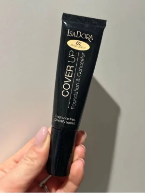 IsaDora Cover Up Foundation 62 Nude - Använd men mycket kvar i. IsaDora Cover Up Foundation & Concealer i färgen 62 Nude Cover. Tuben är svart med guld- och vit text, och innehåller 35 ml. Produkten är parfymfri och kliniskt testad, perfekt för att täcka ojämnheter och ge en jämn finish.