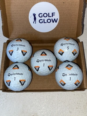 TaylorMade Tp5 Pix 5-pack  - Fem vita golfbollar från TaylorMade med svart och orange mönster, levereras i en brun kartong med Golf Glow-sticker. Perfekta för dig som vill ha snygga och pålitliga bollar till golfbanan.