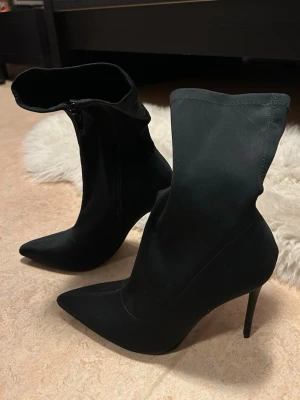 Svarta stövletter, storlek 36 - Svarta spetsiga ankle-boots/halvboots med klack och dragkedja på sidan. Väldigt snygga till både vardag och fest. Endast använda en gång, nyskick. Storlek 36.