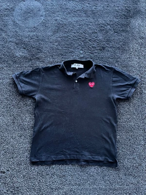 CDG Pike - Svart t-shirt från Comme des Garçons PLAY med klassisk pikékrage och korta ärmar. På bröstet sitter det ikoniska röda hjärtat med ögon. Tillverkad i mjuk bomull och har en clean, stilren look som passar perfekt till jeans eller shorts. Storlek XL men passar M/L, skick 8/10. Pris går att diskutera✅