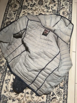 Mörkblå dunjacka från Ulvang - Säljer en mörkblå dunjacka från Ulvang med huva och dragkedjeförsedda fickor. Jackan har quiltad design och tunna kanaler för dunet, vilket ger en smidig och lätt känsla. Perfekt för kalla vinterdagar och enkel att packa ner i väskan.