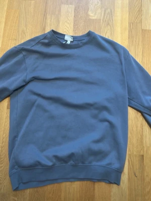 Blå sweatshirt från H&M Essentials - En stilren blå sweatshirt från H&M Essentials, modell No 5, med relaxed fit. Tröjan har rund halsringning, långa ärmar och ribbade muddar vid ärmslut och nederkant. Perfekt för en avslappnad och trendig look.