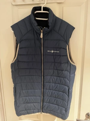 Blå dunväst från Sail Racing - Säljer en snygg blå dunväst från sailracing. Den är i gott skick utan några tydliga tecken på användning. Strl är S och bara att skriva vid minsta lilla.