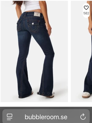 Mörkblå bootcut jeans från Replay - Snygga mörkblå bootcut jeans från True Religion med kontrastsömmar och klassiska fickor bak med lock och knapp. Jeansen har låg midja och utsvängda ben, perfekt för en trendig look. Tuff detalj med True religion på bakfickan.