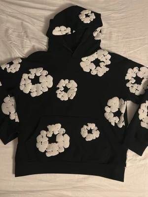 Svart hoodie med vita blommor Denim Tears - Svart hoodie från Denim Tears med stora vita blommönster över hela. Perfekt för dig som vill sticka ut med en unik och trendig stil. Skriv om ni undrar något. Pris går att diskuteras.