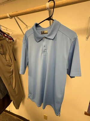 Ljusblå polotopp från Callaway - Säljer en ljusblå polotopp från Callaway med klassisk krage och knappar framtill. Materialet är polyester och har opti-dri teknologi som håller dig torr. Perfekt för dig som gillar sportig stil och vill ha något bekvämt och snyggt.