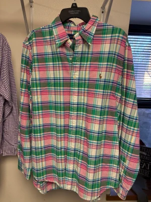 Rutig skjorta från Ralph Lauren XL - Säljer en klassisk rutig skjorta från Ralph Lauren i storlek XL. Skjortan har färger i rosa, grön, blå och vit, med knappar framtill och långärmad design. Materialet är mjuk bomull och den har den ikoniska broderade loggan på bröstet.