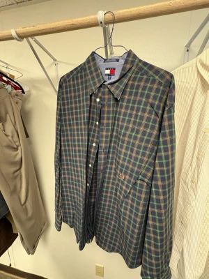 Rutig skjorta från Tommy Hilfiger - Snygg långärmad skjorta från Tommy Hilfiger i mörkblått med grönt, rött och gult rutmönster. Klassisk krage och knappstängning framtill. Bröstficka med diskret logobrodyr. Perfekt för dig som gillar preppy stil.