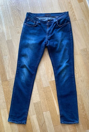 Mörkblå jeans från Nudie Jeans - Snygga mörkblå jeans från Nudie Jeans med klassisk femficksdesign och diskreta slitningar framtill. Bakfickorna har Nudie Jeans signatursöm i svart. Jeansen har smal passform och är tillverkade i stretchigt denimtyg.