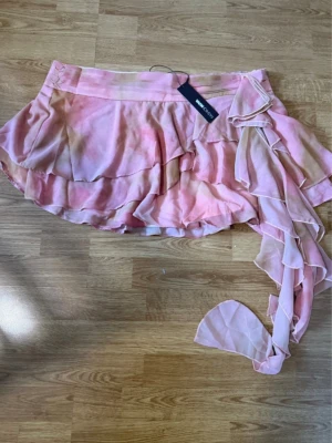 Rosa volangkjol med omlott från fashion nova - Supersöt kort kjol i rosa och beige toner från Gina Tricot. Kjolen har volanger och en lång omlottflik som ger en cool och lekfull look. Perfekt för dig som gillar trendiga detaljer och flowy material.