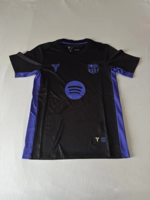 FC Barcelona svart/lila matchtröja - FC Barcelona special edition tröja från denna säsong. Svart/lila design inspirerad av Kobe Bryant med Spotify-logga och klubbmärke. Perfekt för träning, match eller vardag. Bekväm passform i 100% polyester. Storlek S – passar ca 165–175 cm och 50–65 kg. Mått: längd ca 73 cm, bröstvidd ca 47 cm, axelbredd ca 41 cm, ärmlängd ca 23 cm. Helt ny med tagg. Skicka gärna ett meddelande till mig om du har några frågor!