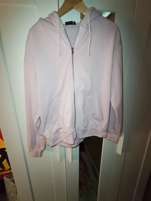 Ljusrosa zip-hoodie med huva - En stilren ljuslila hoodie med dragkedja framtill, huva med dragsko och känguruficka. Mjuk bomullskänsla och ribbade muddar vid ärmslut och nederkant. Perfekt för en avslappnad look.