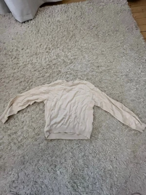 Beige stickad tröja med rund hals - En enkel och stilren beige stickad tröja med rund hals och långa ärmar. Tröjan har ribbade muddar vid ärmslut och nederkant. Perfekt för lager-på-lager och passar till det mesta i garderoben.