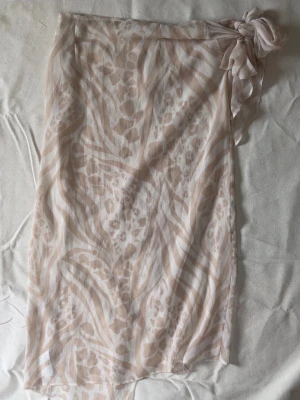 Beige omlott-strandkjol med mönster - Säljer en transparent beige omlott-strandkjol med ljusa djur- och zebramönster. 