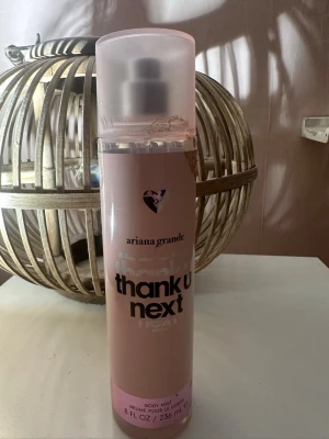 Ariana Grande Thank U Next Body Mist - Fräsch body mist från Ariana Grande i doften Thank U Next. Flaskan är ljusrosa med svart text och har en genomskinlig plastkork. Volymen är 236 ml och designen är modern och trendig, perfekt för dig som gillar söta och fruktiga dofter.