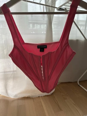 Rosa korsett från PrettyLittleThing - Säljer en snygg rosa korsett från PrettyLittleThing med breda axelband och markerade sömmar framtill. Perfekt för att skapa en trendig siluett.