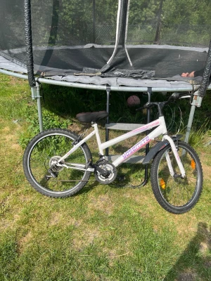 Vit Yosemite cykel med Shimano-växlar - Säljer en vit Yosemite cykel med lila och rosa detaljer. Utrustad med Shimano-växlar och robust ram. Cykeln har svarta däck med grovt mönster, reflexer på hjulen och stänkskärm bak. Passar perfekt för dig som vill ha en smidig cykel till vardags.