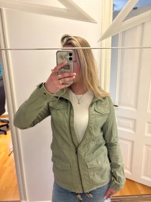 Ljusgrön vindjacka från H&M - Snygg ljusgrön vindjacka från H&M med dragkedja framtill, fyra fickor med lock och justerbar midja med snörning. Jackan har en avslappnad passform och är tillverkad i ett lätt bomullsmaterial. Perfekt för lager på lager och streetstyle.