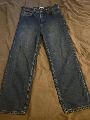 Mörkblå raka jeans - Säljer ett par mörkblå jeans med rak passform och klassisk femficksdesign. Jeansen har hög midja och är tillverkade i kraftigt denimtyg. Perfekta till en avslappnad streetwear-look. Som man ser på första bilden har en bälteshälla har släppt från sömmen baktill (se bild). Går enkelt att sy fast igen!