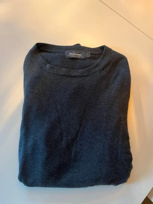 Mörkgrå stickad tröja Dressmann - Mörkgrå stickad tröja från Dressmann med rund halsringning och långa ärmar. Tröjan har en enkel och stilren design, perfekt att matcha med jeans eller chinos. Materialet känns mjukt och bekvämt mot huden.