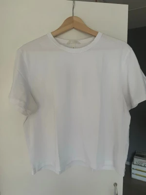 Vit basic t-shirt i bomull - En klassisk vit t-shirt med rund hals och korta ärmar. Tillverkad i mjuk bomull och har en enkel, clean design utan tryck eller detaljer. Perfekt att matcha med allt i garderoben.