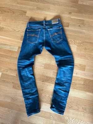 Blå jeans från Nudie Jeans - Snygga blå jeans från Nudie Jeans med klassisk femficksdesign och kontrastsömmar på bakfickorna. Jeansen har en smal passform och är tillverkade i denim med lätt tvättade detaljer för en cool look. Modellen heter tight terry storlek 27/30