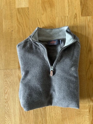 Grå halvzip-tröja från Morris XS - Snygg grå tröja från Morris med halv dragkedja och diskret logga broderad på bröstet. Tröjan har ribbade muddar och krage, perfekt för lager på lager. Tillverkad i mjukt material som känns skönt mot huden. Storlek Xs, egentligen M men den har krympt i tvätten så sitter som en xs