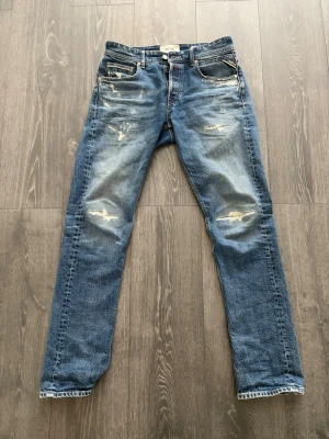 Slitna Replay Jeans - Säljer ett par blå jeans från Replay med snygga slitningar och distressed detaljer på både fram- och baksida. Den är straight fit och är väldigt sköna. Enbart använt fåtal gånger. Storlek 31(W), 32(L). Nypris på ca 2200kr!