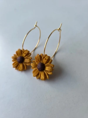 Handgjorda örhängen - solrosor på hoops - Underbara solrosor i senapsgul, lätt skimrande färg på tunna guldfärgade ringar med en diameter på 2,5cm. Blommorna har detaljerade kronblad och en mörkbrun mitt. Gjorda för hand av mig i polymerlera. 