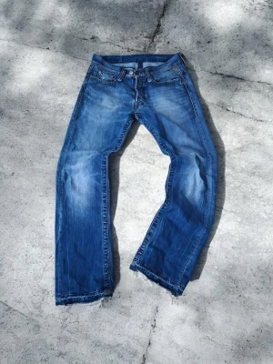 Replay ,Blå slitna jeans med rå kant - Ett par blå jeans med tvättad look och slitningar, raka ben och råa, fransiga benslut. Klassisk femficksmodell i denim med dragkedjegylf. Perfekta för en avslappnad och trendig stil.