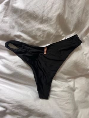 Svart bikiniunderdel NLY Beach - Säljer en svart bikiniunderdel från NLY Beach i vad jag tror är strl M (men står ej). Modellen har en hög skärning och smala sidor för en trendig look. Materialet är mjukt och stretchigt, perfekt för lata dagar på stranden eller vid poolen. Fint skick, knappt använd och självklart rengjord ordentligt.