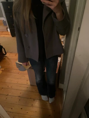 Grå kappa från Gina Tricot - Stilren grå kappa från Gina Tricot med rak passform och stora knappar framtill. Kappan har en klassisk krage och är tillverkad i ett mjukt tyg som ger en snygg look till hösten och vintern. Perfekt att matcha med jeans eller kjol.