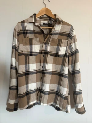 Beige och vit rutig skjorta - ”Avicii skjorta” Snygg rutig skjorta i beige, vitt och svart med två bröstfickor och knappar framtill. Perfekt för en avslappnad och trendig look. Använts 2 gånger så inga slitage eller några konstigheter😀
