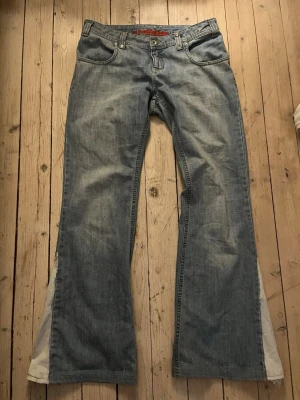 Ljusblå bootcut jeans från Rednap - Säljer ett par ljusblå bootcut jeans från Rednap med klassisk femficksmodell och snygga slitningar. Jeansen har normal midja, bälteshällor och dragkedjegylf. Perfekta för dig som gillar en avslappnad och retro look. Midjemått: 42cm
