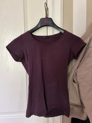 Vinröd t shirt - En enkel och stilren vinröd/lila t-shirt med rund halsringning och korta ärmar. Tillverkad i mjukt material som känns skönt mot huden. Perfekt att matcha med jeans eller kjol för en avslappnad look.