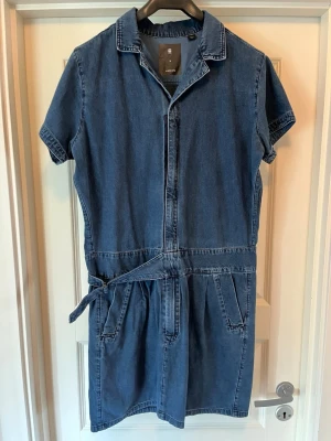 Blå jeansklänning g star  - Snygg blå jeansklänning med korta ärmar, krage och midjeband i midjan. Klänningen har fickor både fram och bak samt en avslappnad passform. Perfekt för dig som gillar en enkel och stilren look. Storlek M märke g star 