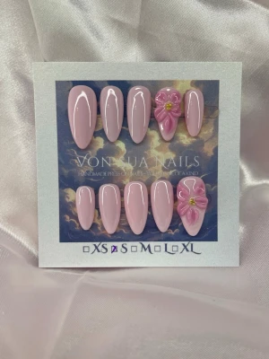 PinkLily (S);Medium Almond - Snygga handgjorda press-on naglar i ljusrosa med glansig finish och medium lång almondform. Två av naglarna har handgjorda 3D-blommor i rosa med guld detalj i mitten för extra wow-effekt. Perfekt för dig som vill ha något unikt och trendigt. Handgjorda och riktigt detaljerade.S: 15 mm, 11,5 mm, 12 mm, 11 mm, 9 mm 